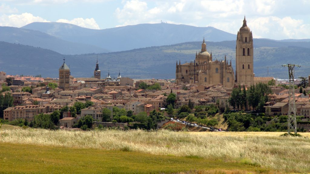 Vista panorámica del antiguo Acueducto Romano en Segovia, con sus arcos de piedra dobles perfectamente alineados, extendiéndose a través de la ciudad, y el imponente Alcázar de Segovia al fondo, reminiscente de un castillo de cuentos de hadas.